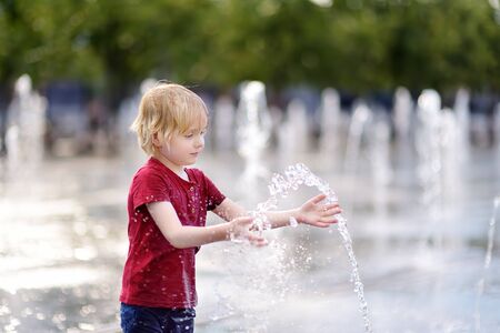 Little boy plays in the square between the water jets in the fountain at sunny summer day. Active summer leisure for kids in the city.の写真素材