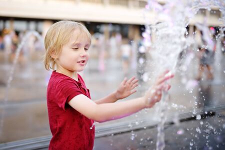 Little boy plays in the square between the water jets in the fountain at sunny summer day. Active summer leisure for kids in the city.の写真素材