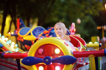 Little boy having fun on attraction in public park. Child riding on a merry go round at summer evening. Attraction, planes, cars, illumination, fun... Entertainment industry.の写真素材