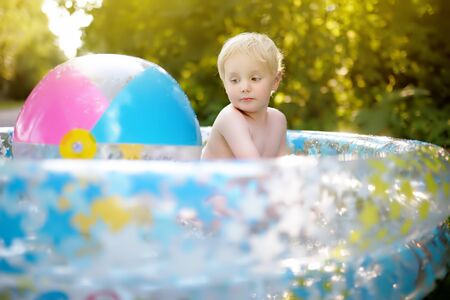 Cute little boy swimming in a inflatable pool outdoors on the backyard. Outdoors summer activities for kids.の写真素材