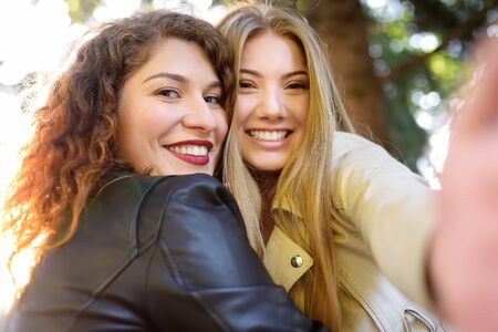 Two beautiful young women take selfie on sunny park. Girlfriends. Communication and gossip.