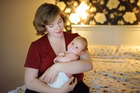 Young mother with newborn baby sitting on bed at home