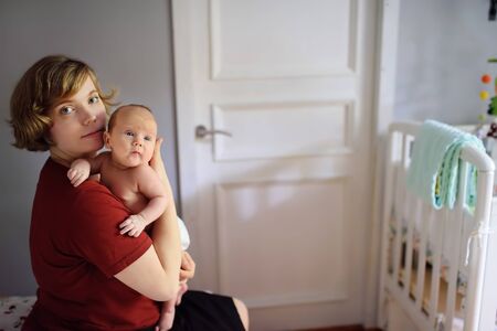 Young mother with newborn baby sitting on bed at homeの写真素材