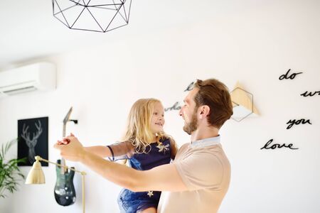 Young handsome father with his little curly hair daughter dancing at home. Loving dad and his...