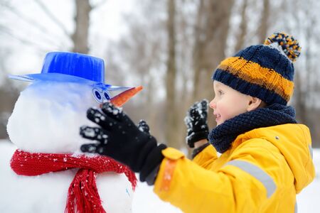 Little boy playing with funny snowman. Active outdoors leisure with children in winter. Kid during stroll in a snowy winter parkの写真素材