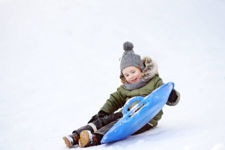 Little boy enjoy riding on ice slide in winter. Outdoor winter activities for family with kids.の写真素材