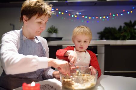 Merry little boy and his mother or young grandmother bake cookies together during the holidays...