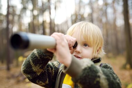 Little boy scout with spyglass during hiking in autumn forest. Child is looking through a spyglass. Concepts of adventure, scouting and hiking tourism for kids.の写真素材