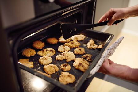 Woman is taking baking tray with christmas cookies from oven. Cooking of biscuits for Xmas holidays.