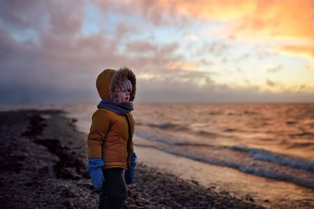Little child is walking on Baltic Sea coast on sunset of winter day. Outdoors activity for family with kids in winter. Estonia.の写真素材