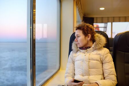 Mature woman is looking on the window at the amazing view of frozen sea during crossing on the ferry...