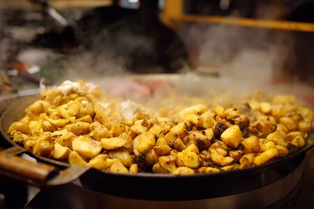 Hot food on Tallinn Christmas fair. Fried potatoes in large kitchen pan. Street food.の写真素材