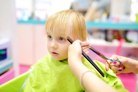 Preschooler boy getting haircut. Children hairdresser with professional tools - comb and scissors. Cutting hair for kids.の写真素材