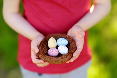 Pretty little boy holding nest with easter eggs in spring park on Easter day. Traditional easter festival outdoors.の写真素材