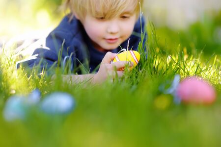 Little boy hunting for egg in spring garden on Easter day. Traditional easter festival outdoors. Focus on multicolor eggs.の写真素材