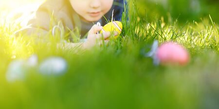 Little boy hunting for egg in spring garden on Easter day. Traditional easter festival outdoors....