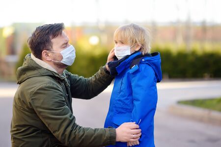Mature man wearing a protective mask puts a face mask on a his son in airport, supermarket or other public place. Safety during COVID-19 outbreak. Epidemic of virus covid.の写真素材