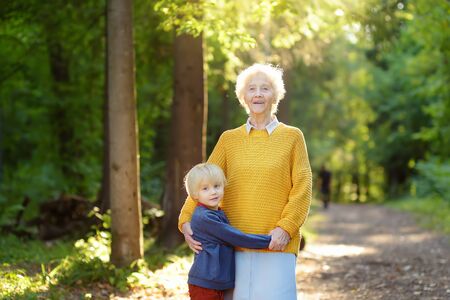Loving grandson tenderly embracing his joyful elderly grandmother during walking at summer park. Two generations of family.の写真素材
