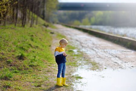Preschooler child wearing yellow rain boots walking near river after rain. Kid playing and having fun in sunny spring or summer day. Outdoors games for children.の写真素材