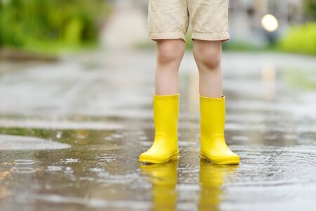 Little boy wearing yellow rubber boots walking on rainy summer day in small town. Child having fun. Outdoors games for children in rain.の写真素材