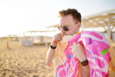 Man wearing sunglasses inflates an inflatable donut swimming circle on the seashore. Summer holidays on sea for families with kids. Fun beach vacation.の写真素材