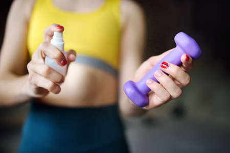 Girl cleaning of sport equipments of gym with disinfecting spray. Woman making disinfection of...