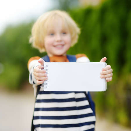 Happy little boy with backpack going to school. Child holding with hands empty white blank card for copy space and free text. Space for your advertising or information.の写真素材