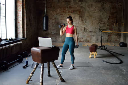 Sportswoman trainer leads online fitness class. Woman stretching or yoga in gym using a laptop with online training. Regular sports boosts immune system and promote good health and resistance to diseases. Healthy lifestyleの写真素材