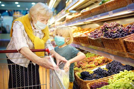 Senior woman and her grandchild wearing disposable medical mask shopping in grocery supermarket during coronavirus pneumonia outbreak. Protection and prevent measures for family while epidemic time.の写真素材