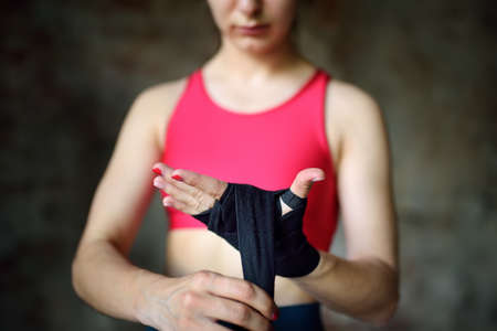 Young female boxer preparing for boxing fight. Athletic woman wearing strap on wrist before boxing practice in gym. Regular sports boosts immune system and promote good health and resistance to diseasesの写真素材