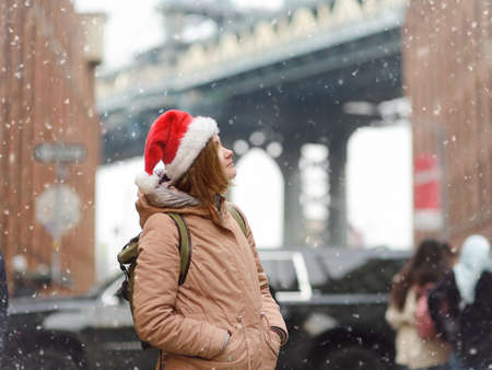 A young woman tourist in a Santa Claus hat walks during a snowfall in New York on Christmas Eve....