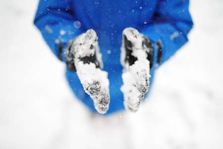Little boy walking and having fun playing with fresh snow during snowfall. Snowball fight. Close-up of gloves with snow. Active leisure outdoors for kids on nature in snowy winter day.の写真素材