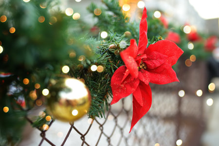 Close-up photo of Christmas and New Year decorations. Fence decorated with a garland of artificial fir branches with red flowers. Outdoors Xmas decorationsの写真素材