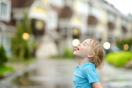 Little boy walking on rainy summer day in small town. Child having fun. Kid catches raindrops with tongue. Outdoors games for children in rain.の写真素材