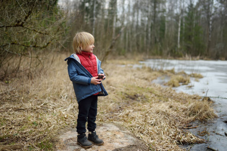 Little boy playing on shore of forest lake on early spring day. Outdoor activity for kids. Beauty of...