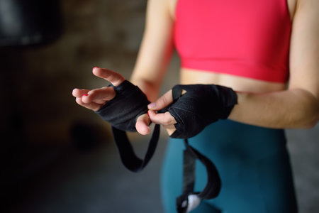 Young female boxer preparing for boxing fight.Athletic woman wearing strap on wrist before boxing practice in gym.Regular sports boosts immune system and promote good health and resistance to diseasesの写真素材