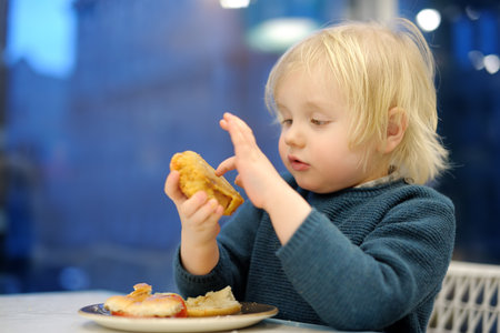 Cute preschooler boy eating large hamburger at fast food restaurant. Unhealthy meal for kids. Junk food. Overweight problem childrenの写真素材