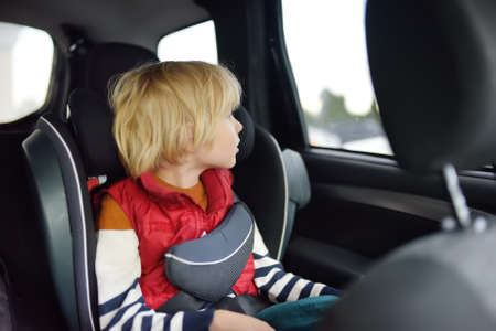 Cute preschooler boy sitting in a car seat and wearing a belt. ? hild is looking out the window of a car during a family trip. Safety of transportation of children.の写真素材