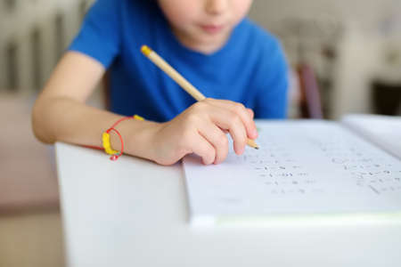 Elementary student boy doing homework at home. Child learning to count, solves arithmetic examples, doing exercises in workbook. Math tutorial. Preparing preschooler baby for school.Education for kidsの写真素材