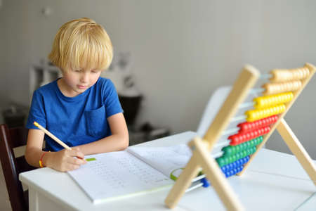 Elementary student boy doing homework at home. Child learning to count, solves arithmetic examples,...