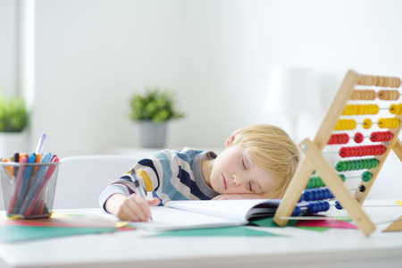 Elementary student boy fell asleep while doing homework at home. Overloading children. Preparing preschooler baby for school. Education for kidsの写真素材