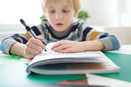 Elementary student boy doing math homework at home.Child learning to count, solves arithmetic...