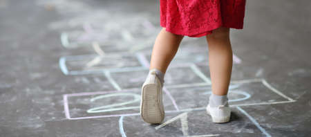 Closeup of little girl's legs and hop scotch drawn on asphalt. Child playing hopscotch game on playground outdoors on a sunny day. Summer activities for children.の写真素材
