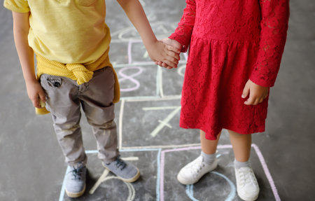Little boy and girl on background hopscotch which drawn on asphalt. Children playing hop scotch game on playground outdoors on a sunny day. Kids having fun. Summer activities for children. Best friendsの写真素材