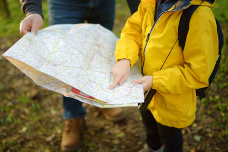 Schoolchild and his mature father hiking together and exploring nature. Little boy with dad looking map during orienteering in forest. Adventure, scouting and hiking tourism for kids. Daddy and sonの写真素材