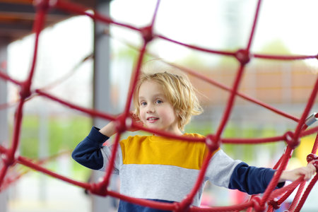Cute preschooler boy having fun on outdoor playground. Spring / summer / autumn active sport leisure for kids. Activity for family with children. Equipment of entertainment park for kids.の写真素材