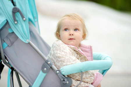 Adorable toddler girl is riding into baby stroller during stroll. Active leisure and walking for...