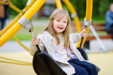 Little girl having fun on outside playground. Spring / summer / autumn active sport leisure for kids. Child on swing. Outdoor activity for children. Equipment for playground and entertainment parkの写真素材