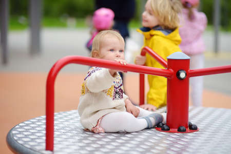 Toddler girl having fun on outdoor playground. Preschooler brother rides younger sister on carousel. Friendship of siblings. Spring / summer / autumn active sport leisure for kids. Activities for childrenの写真素材