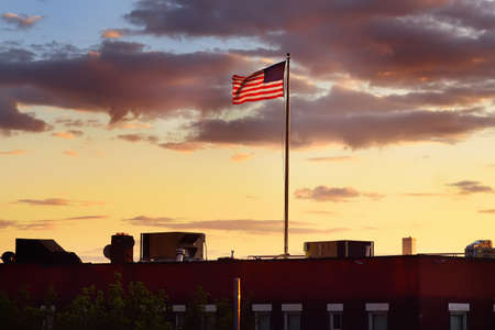 Flag of USA waving on roof top of building on background of summer sunset sky. The fourth of July is Day of Independence of United States of America.の写真素材